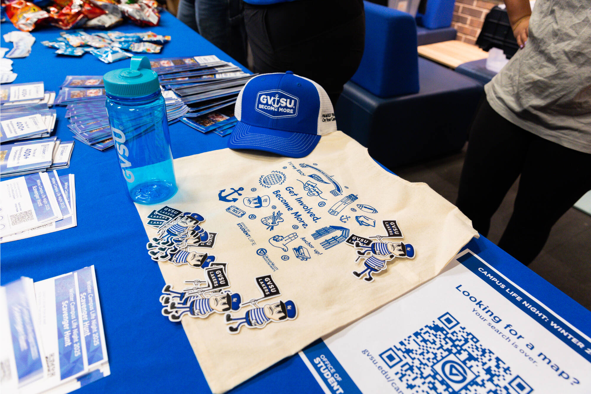 A GVSU tote bag, Louie the Laker stickers, GVSU hat, and GVSU water bottle displayed on a blue table